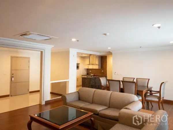 Condominium for rent in Watthana, Bangkok - Open-plan living and dining area with sofa set, dining table and adjoining kitchen, warm wood floors and recessed lighting.