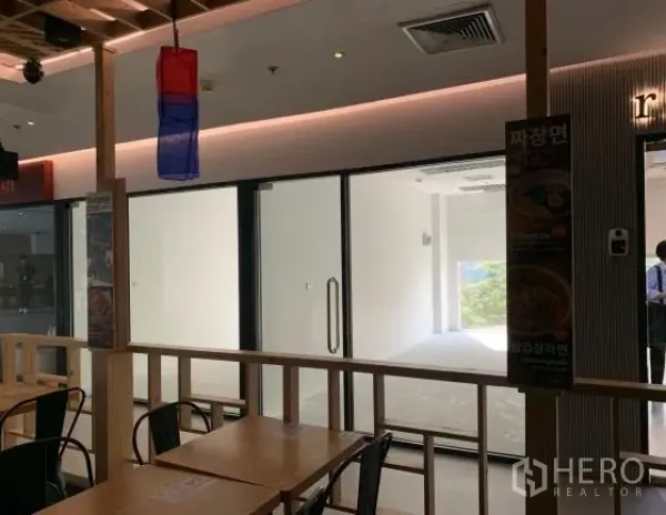 零售空间 出租在Bang Rak, Bangkok - 玻璃门面店铺面向商场内用餐区，可见天花灯与指示牌。