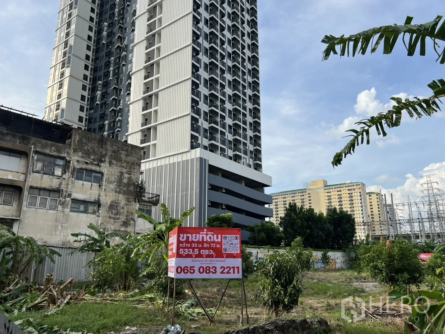 Land for sale in Suan Luang, Bangkok - Street‑level view of the developable plot with a sale board and an adjacent high‑rise condominium.