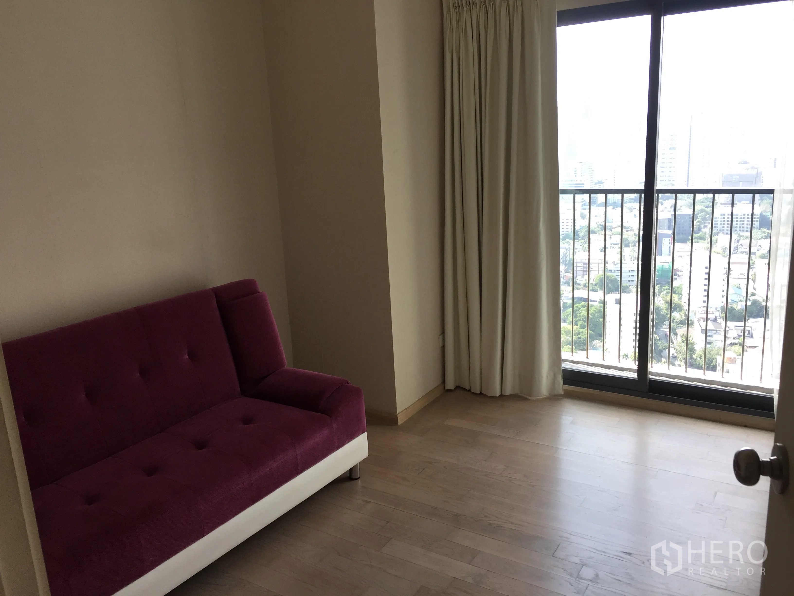Condominium for rent in Khlong Toei, Bangkok - Bright room with purple sofa and sliding doors to a balcony with Bangkok skyline view.