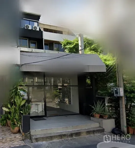 店屋 出租在Watthana, Bangkok - 带玻璃门面与雨棚的商用联排入口，两侧摆放绿植