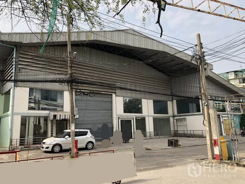 Warehouse for rent in Suan Luang, Bangkok - Street view of the warehouse exterior with two roller shutters, glass frontage and parking bay.