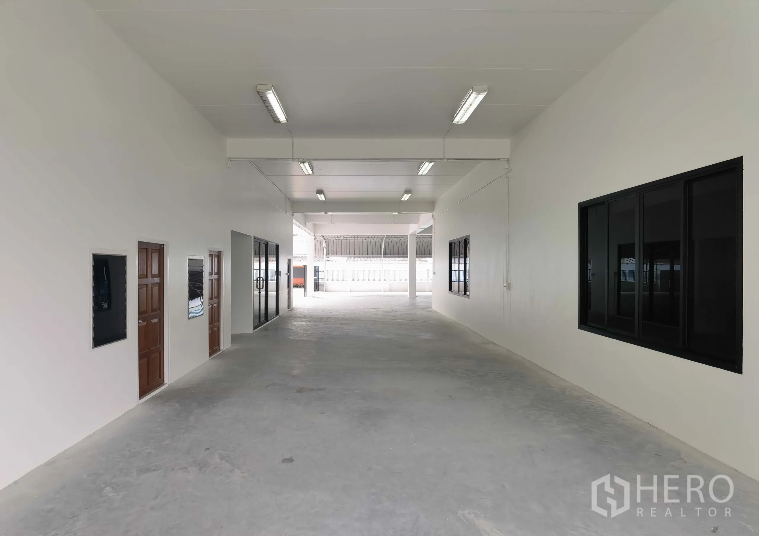 Warehouse for rent in Samut Prakan - Clean internal corridor with offices and glass doors, fluorescent lighting and smooth concrete flooring.