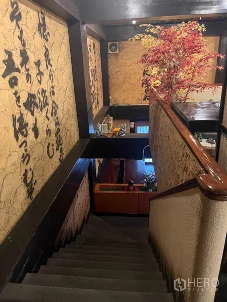 Shophouse for rent in Khlong Toei, Bangkok - Staircase with wood handrail, calligraphy wall panels, and decorative maple tree.