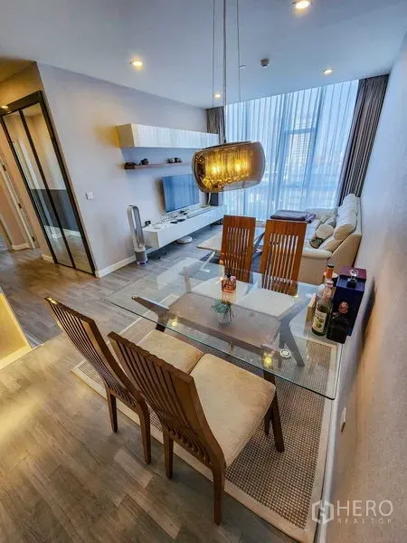 Condominium for rent or sale in Bang Rak, Bangkok - Open-plan dining and living area with a glass table, pendant light, and floor-to-ceiling windows.