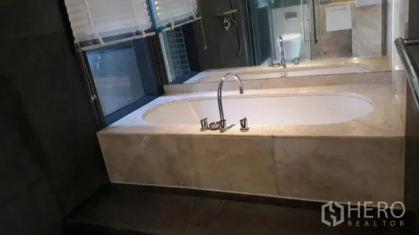 Condominium for sale in Sathon, Bangkok - Bathroom with large built-in bathtub, marble surround and wide mirror.