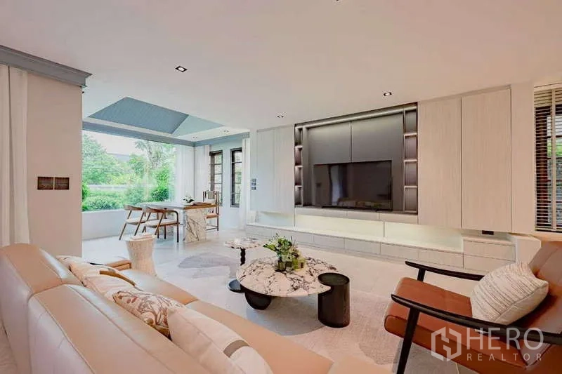 Detached House for rent or sale in Phra Khanong, Bangkok - Living area facing a feature TV wall with large windows opening to the green lawn.