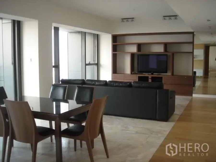 Condominium for rent in Sathon, Bangkok - Open-plan living and dining area with black sofa, built-in TV wall and floor-to-ceiling windows.
