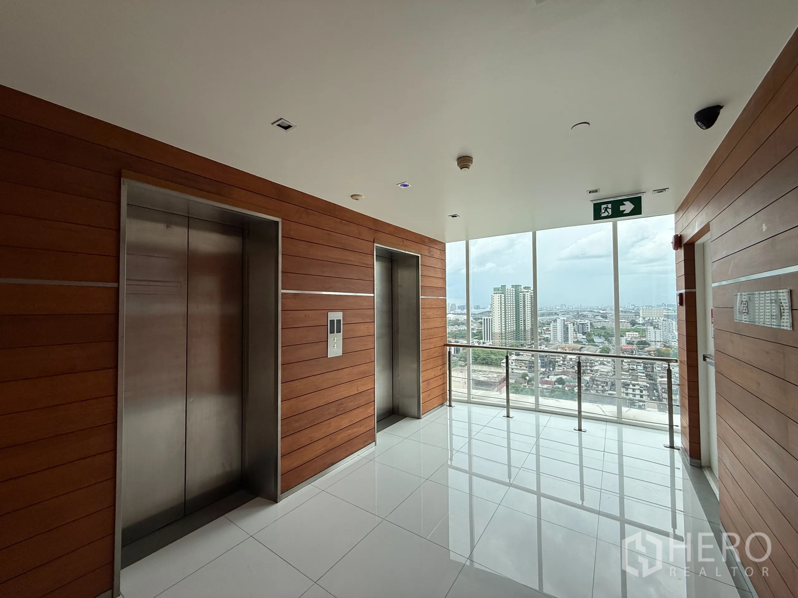 Condominium for rent in Phaya Thai, Bangkok - Elevator lobby with wood‑panel walls, two stainless lifts and large windows framing the city.