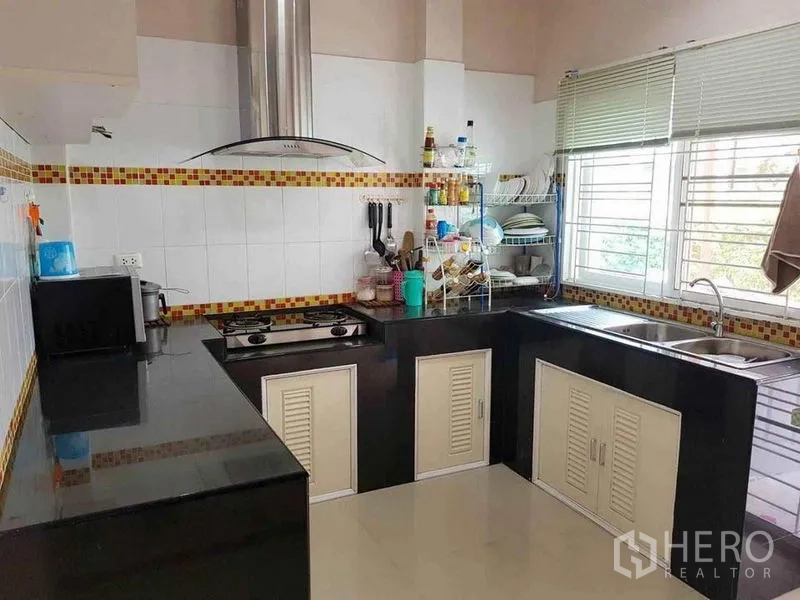 Detached House for sale in Nonthaburi - U-shaped kitchen with black countertops, gas hob, stainless hood and a large window.