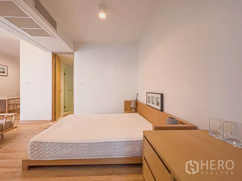 公寓 出售在Watthana, Bangkok - 卧室朝客厅的视角，可见斗柜、床头灯及浴室门口。
