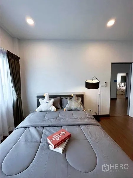 独立式住宅 出租或出售在Bang Phli, Samut Prakan - 次卧配灰色床品、落地灯与窗帘。