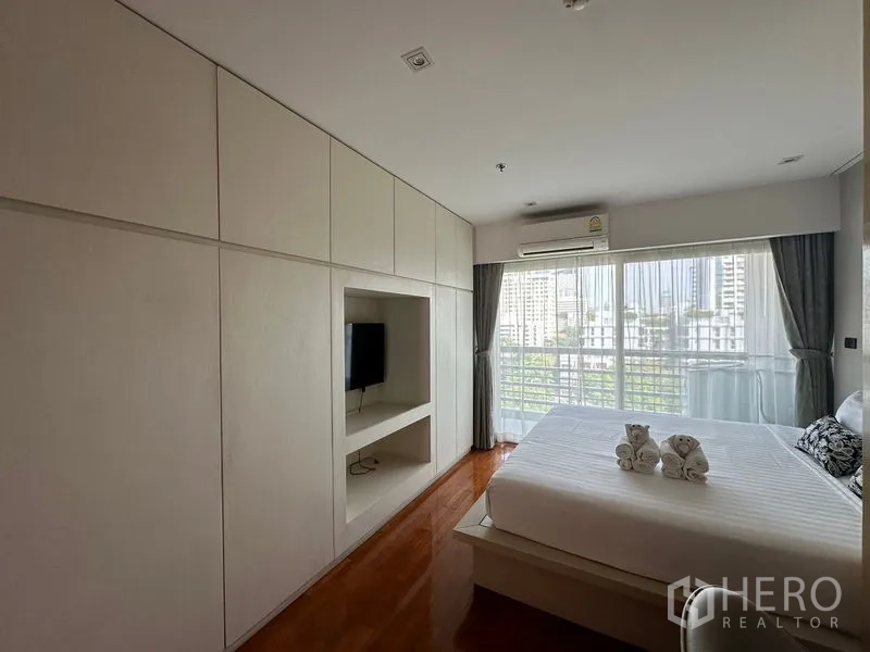 Apartment for rent in Khlong Toei, Bangkok - Bedroom with full-height wardrobes, built-in TV niche, and floor-to-ceiling windows.