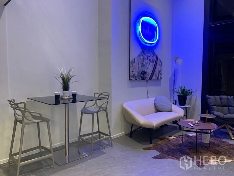 Condominium for rent in Bang Rak, Bangkok - Loft-style living area with high ceiling, compact sofa, dining set and neon wall art.