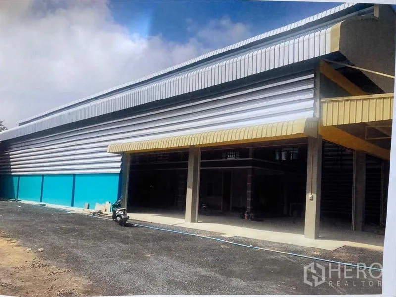 货栈 出租在Bang Pakong, Chachoengsao - 日间外观，带金色雨棚的金属板仓库与宽阔车道。