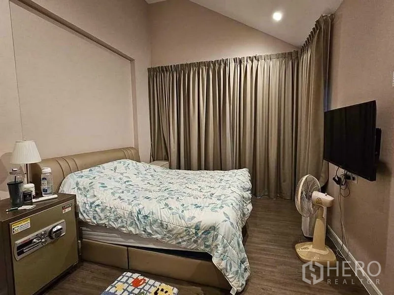 Detached House for sale in Bang Kruai, Nonthaburi - Cozy bedroom with high ceiling, full-length curtains, wall-mounted TV and bedside cabinet.