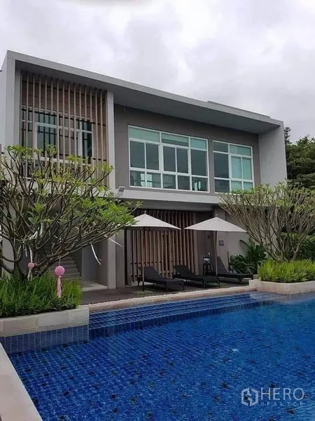 Detached House for rent or sale in Saphan Sung, Bangkok - Resident clubhouse with outdoor swimming pool, deck chairs and greenery.