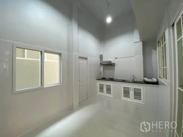 Townhouse for rent in Bang Na, Bangkok - High‑ceiling Thai kitchen with long countertop, gas hob, extractor, and white cabinetry.
