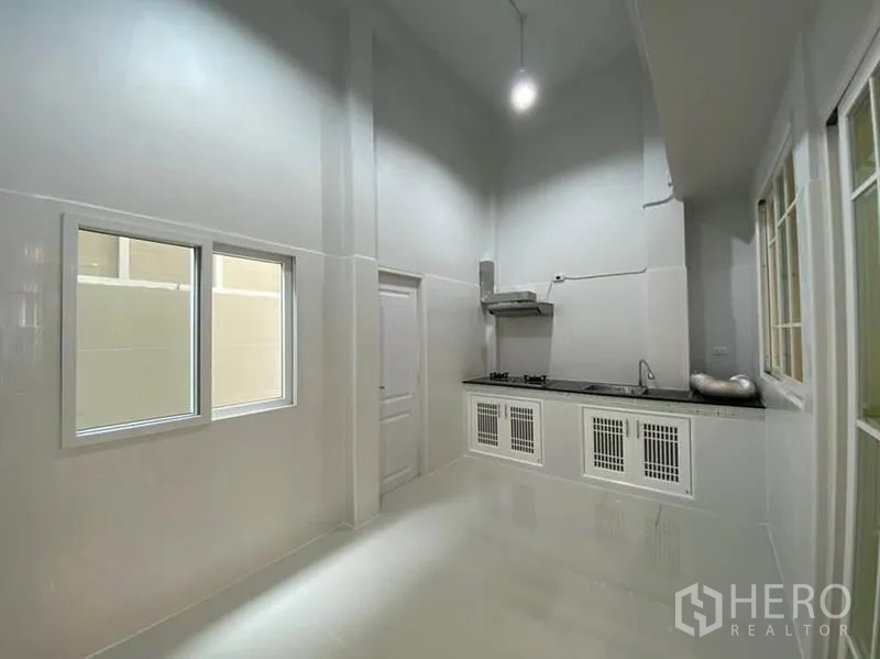 Townhouse for rent in Bang Na, Bangkok - High‑ceiling Thai kitchen with long countertop, gas hob, extractor, and white cabinetry.