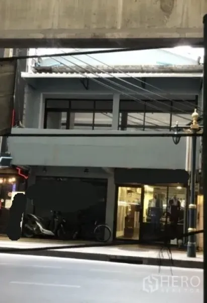 Shophouse for rent in Khlong Toei, Bangkok - Street-facing shophouse exterior with wide glass storefront beneath an elevated transit line on Sukhumvit.