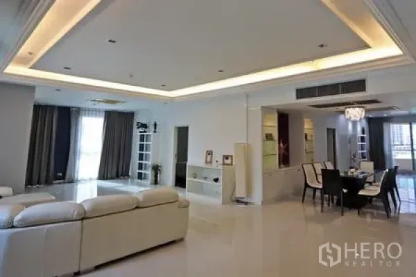 公寓 出租在Watthana, Bangkok - 明亮的客餐一体空间，层级吊顶灯、白色沙发，并可通往阳台。