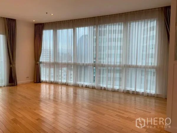 Condominium for rent in Khlong Toei, Bangkok - Wall of windows with city view and wooden floors in an open-plan lounge.