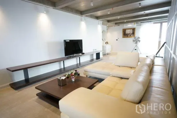 Condominium for rent or sale in Bang Na, Bangkok - Spacious living room with cream L‑shaped sofa, long media shelf and ceiling spotlights.