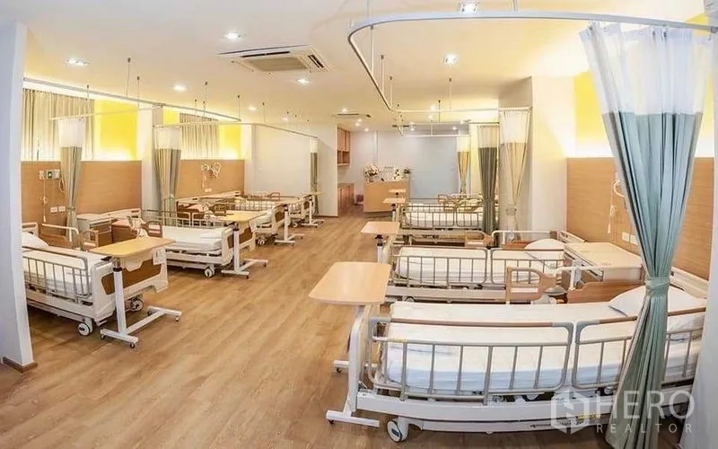 零售空间 出租在Bang Kapi, Bangkok - 病房式空间另一角，带万向轮病床、床旁桌、暖色照明与分隔帘