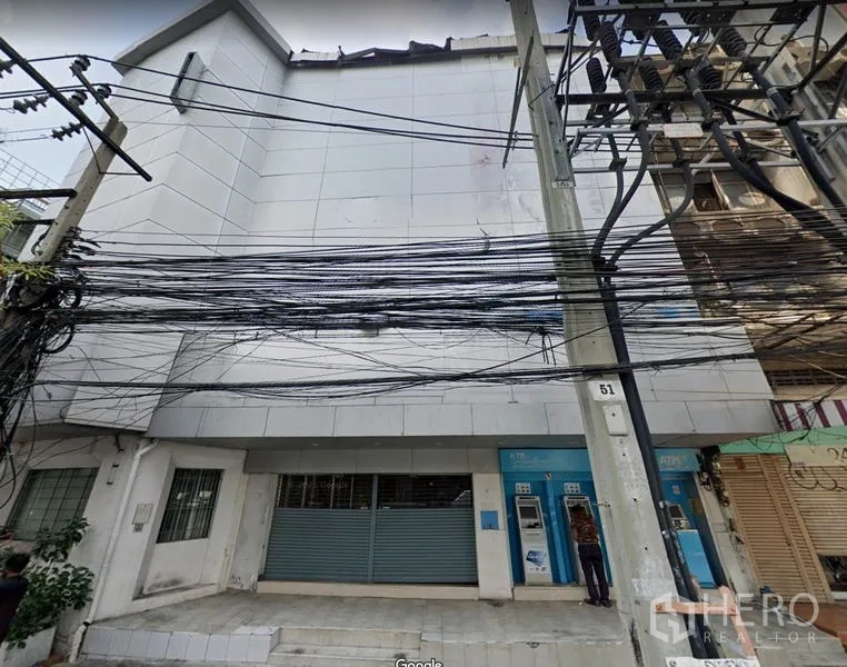 Shophouse for rent or sale in Khlong Toei, Bangkok - Street view of a multi-storey shophouse facade with metal roller shutter and dense power lines in Phra Khanong.