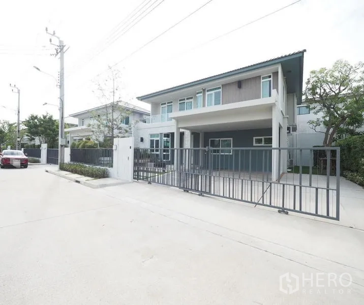 独立式住宅 出租在Prawet, Bangkok - 外观斜角视图，宽敞车道与滑动金属门，社区街道安静。