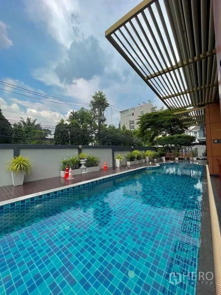 公寓 出租在Watthana, Bangkok - 户外蓝色马赛克泳池，池畔平台与绿植，天空开阔。