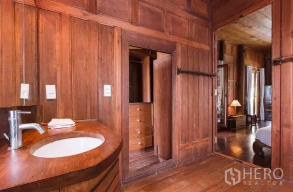 Detached House for rent in Bang Na, Bangkok - Wood‑clad bathroom with curved wooden vanity, mirror, and doorway to bedroom with built‑in closet.