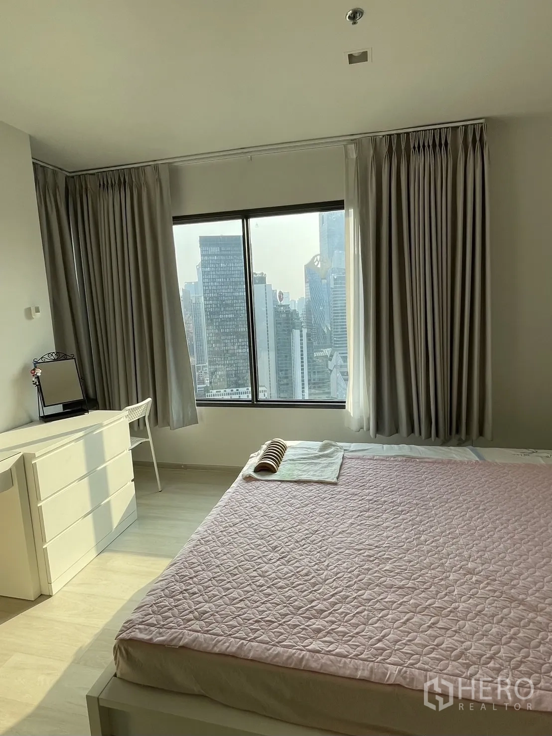 公寓 for rent in Pathum Wan, Bangkok - 宽敞卧室，大窗与粉色床品，五斗柜，面向城市景观。