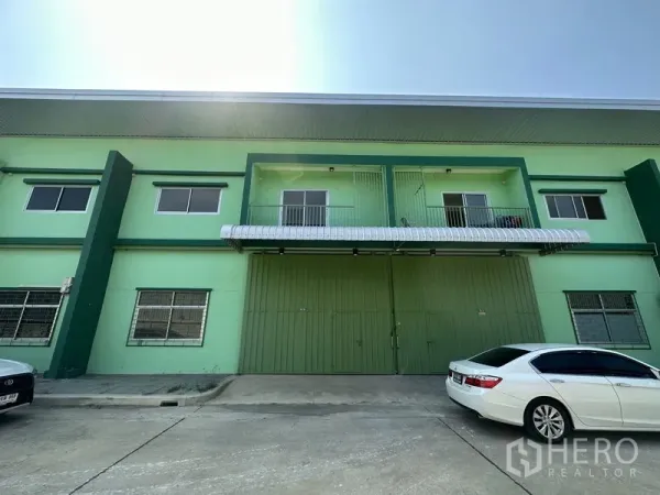 货栈 出租在Pathum Thani - 绿色两层仓库外立面，超大钢制双开门与前方停车区。