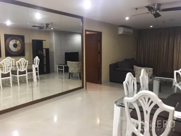 Condominium for rent in Watthana, Bangkok - Open-plan living and dining area with a mirrored wall and glass dining table.