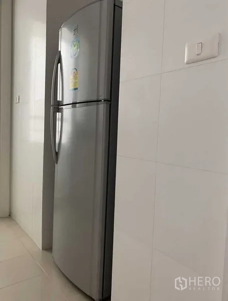 Condominium for rent in Khlong Toei, Bangkok - Tall stainless steel refrigerator set against clean white tiled kitchen walls.