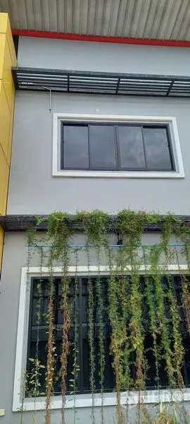 Warehouse for rent or sale in Krathum Baen, Samut Sakhon - Second-floor windows and yellow accent panel on contemporary warehouse exterior with vertical greenery.