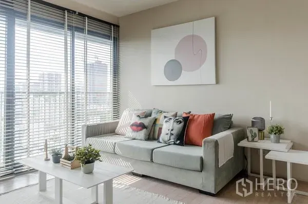 Condominium for rent in Watthana, Bangkok - Cozy lounge with soft grey sofa, coffee table and balcony windows, minimalist decor.