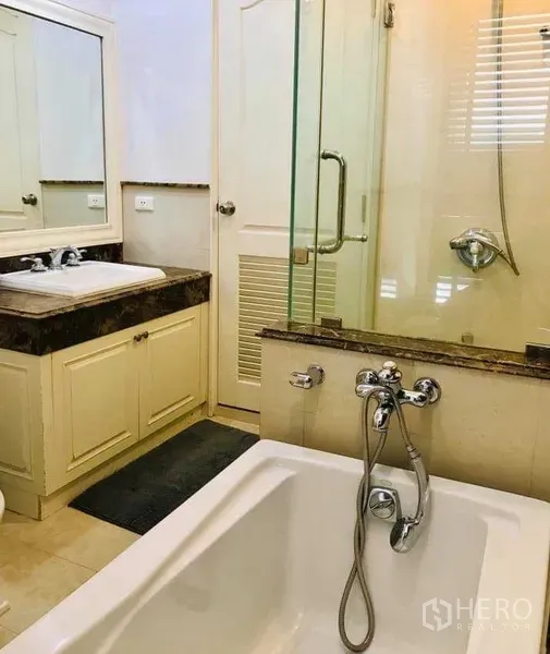 Condominium for rent in Khlong Toei, Bangkok - Secondary bathroom featuring a soaking bathtub, stone-top vanity and glass shower enclosure.