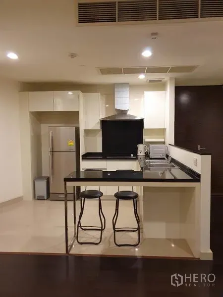 公寓 出租在Khlong San, Bangkok - 现代厨房，白色柜体、黑色台面，吧台配高脚凳，不锈钢冰箱。