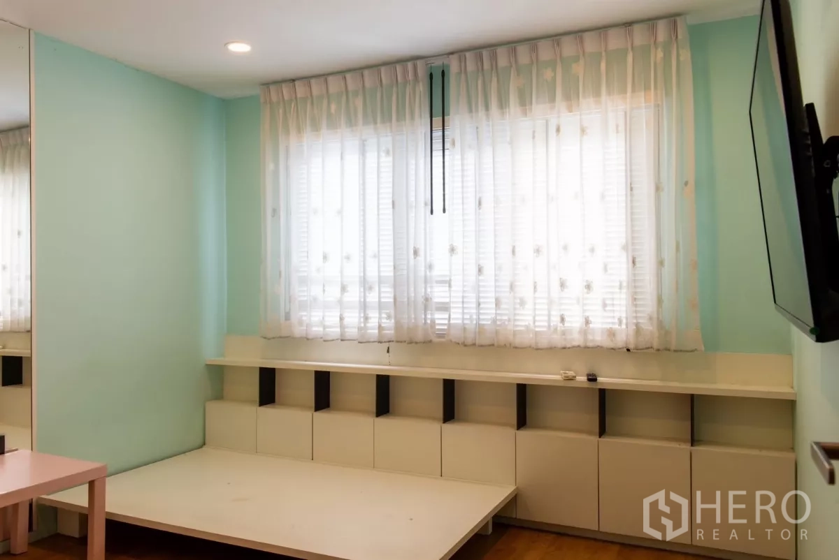 Townhouse for rent in Lat Phrao, Bangkok - Light-filled bedroom with mint walls, sheer curtains and low platform.