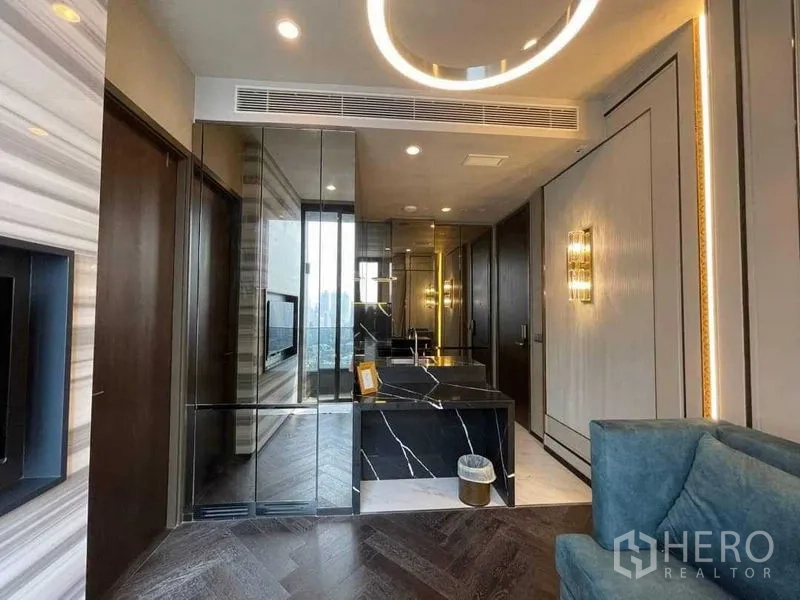 Condominium for rent in Khlong Toei, Bangkok - Entry to the living area with herringbone wood flooring, mirrored walls and a marble island counter.