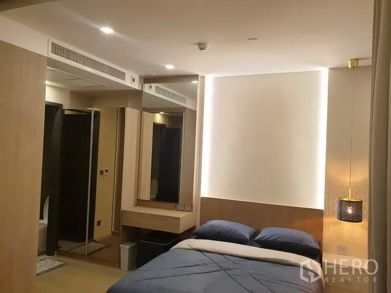 Condominium for rent in Watthana, Bangkok - Cozy bedroom with bed, vanity, mirrored wardrobe and entrance to the bathroom.