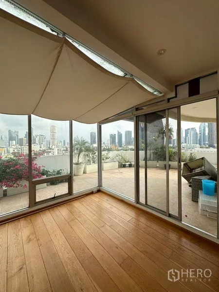 Condominium for rent in Khlong Toei, Bangkok - Sunroom corner with floor-to-ceiling windows leading to an expansive terrace and city skyline.