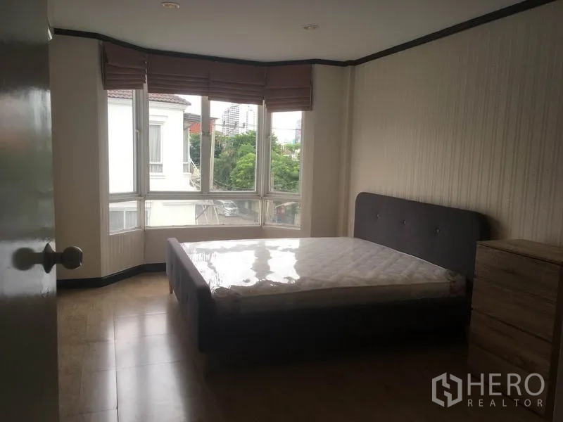 Townhouse for rent in Din Daeng, Bangkok - Master bedroom with bay window, greenery views, queen bed and wooden flooring.