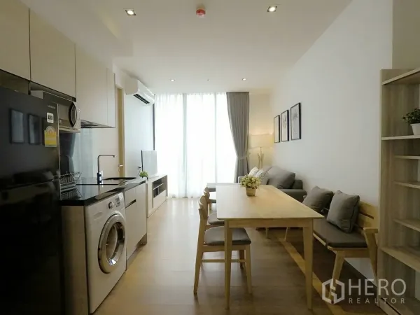 Condominium for rent or sale in Khlong Toei, Bangkok - Open-plan living, dining, and kitchen with sofa, dining table, built-in cabinets, and washing machine.