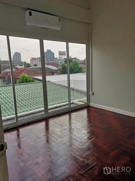 Townhouse for rent or sale in Din Daeng, Bangkok - Bedroom with large sliding doors to a balcony, air conditioner, and neighborhood rooftop views.
