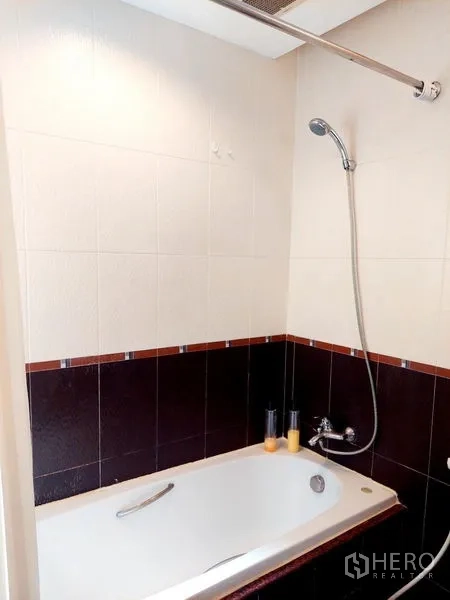 Apartment for rent - Close-up of bathtub with shower fixture and half-height wall tiles.