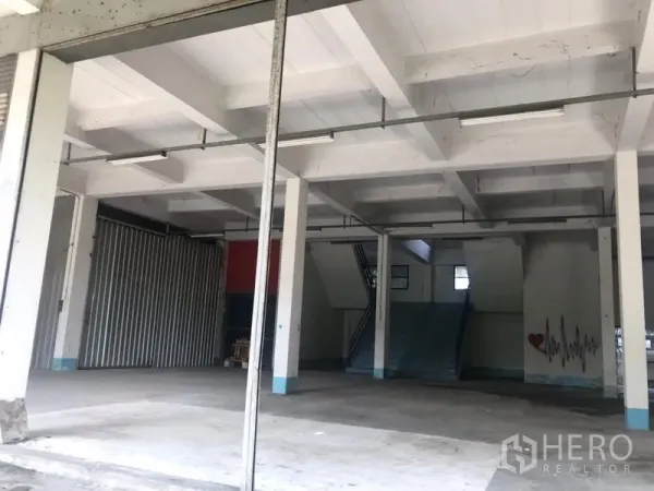Warehouse for rent in Bueng Kum, Bangkok - Open-plan warehouse interior in Bueng Kum with high ceilings, concrete floors, support columns, stairway to mezzanine and fluorescent strip lighting.
