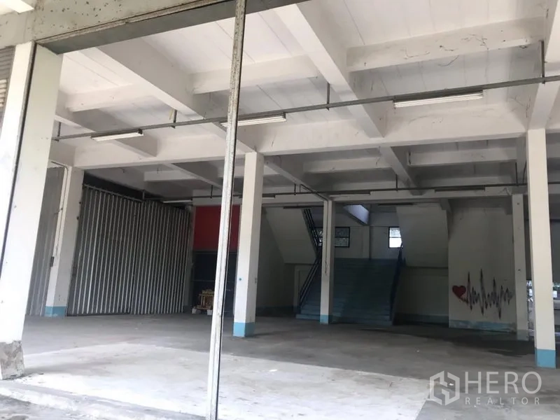 Warehouse for rent in Bueng Kum, Bangkok - Open-plan warehouse interior in Bueng Kum with high ceilings, concrete floors, support columns, stairway to mezzanine and fluorescent strip lighting.